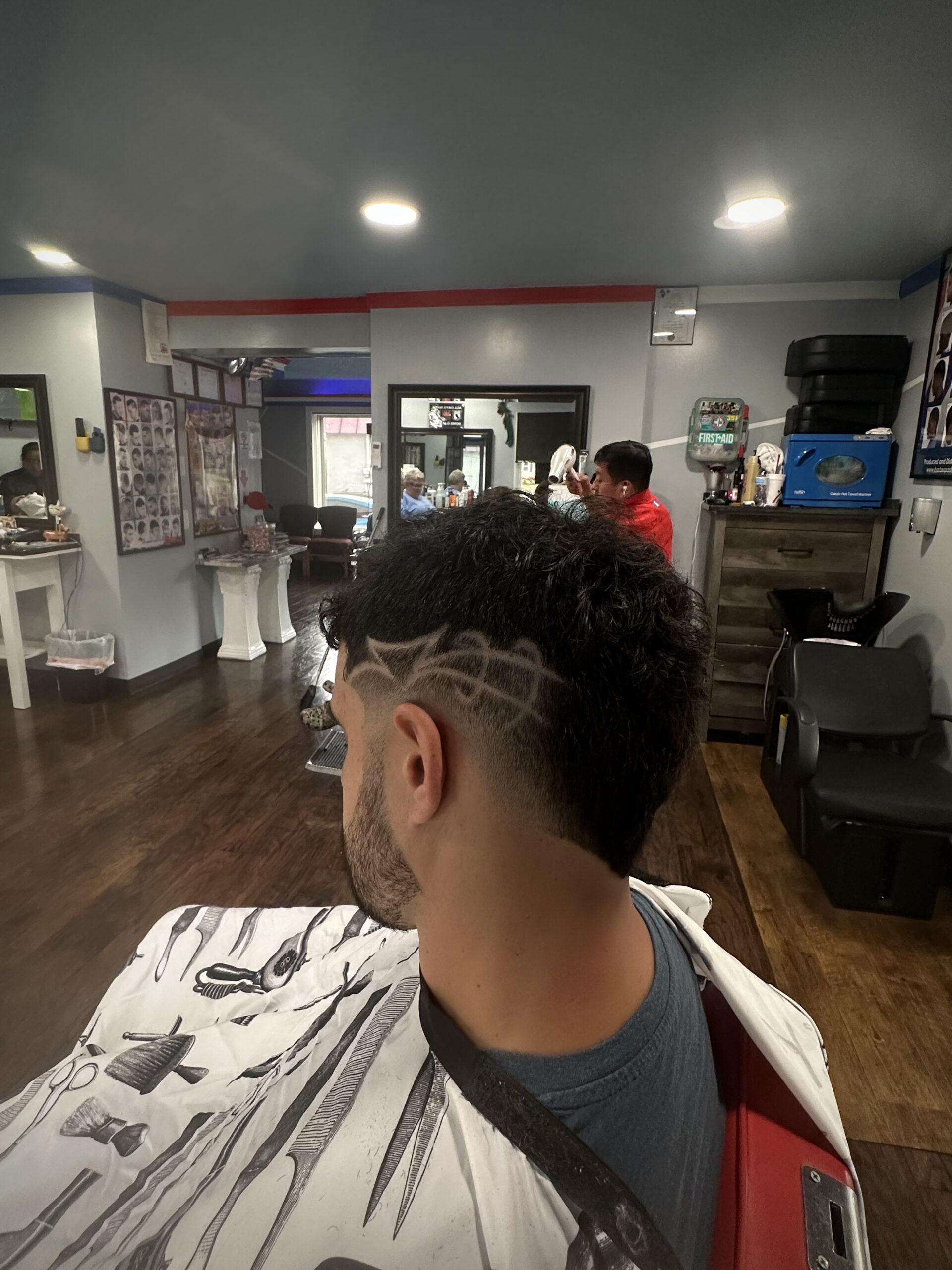 A man in a barber shop with a geometric design shaved into the side of his hair. The modern interior features wooden floors and bright lighting.